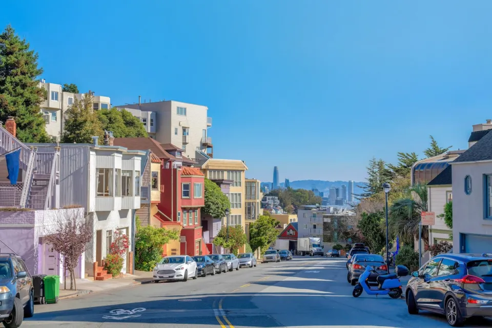 View down San Francisco street with colorful residential buildings and high-rise downtown buildings in distance.